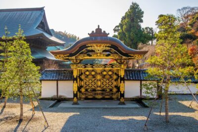 建長寺の唐門。黒漆に金の飾り金具が施された門と、白い築地塀、松の木